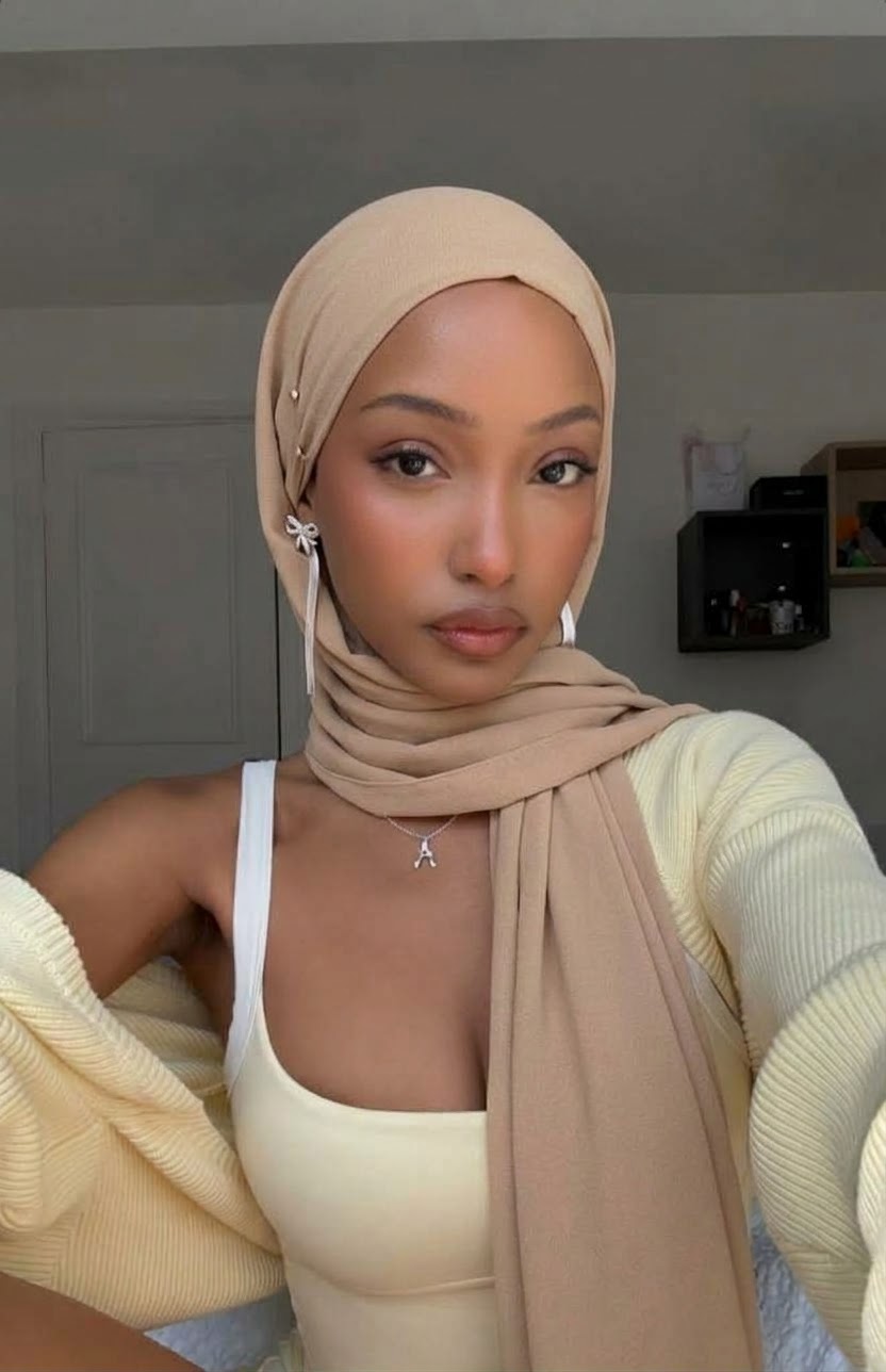 Beige hijab and white tank top with a cream knit cardigan draped off the shoulders in an indoor selfie.