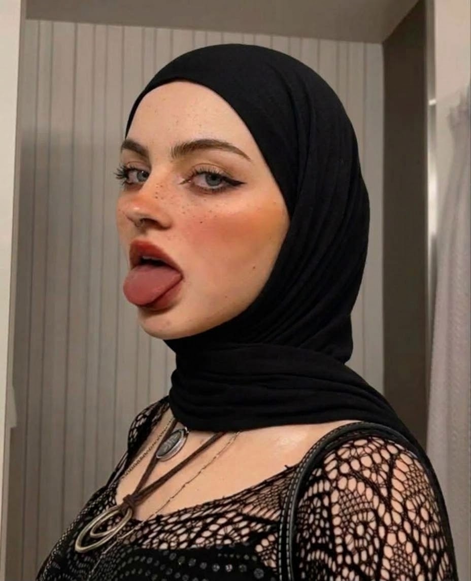 Black hijab and black lace top with crossed neckline ties in a tongue-out side-pose selfie.
