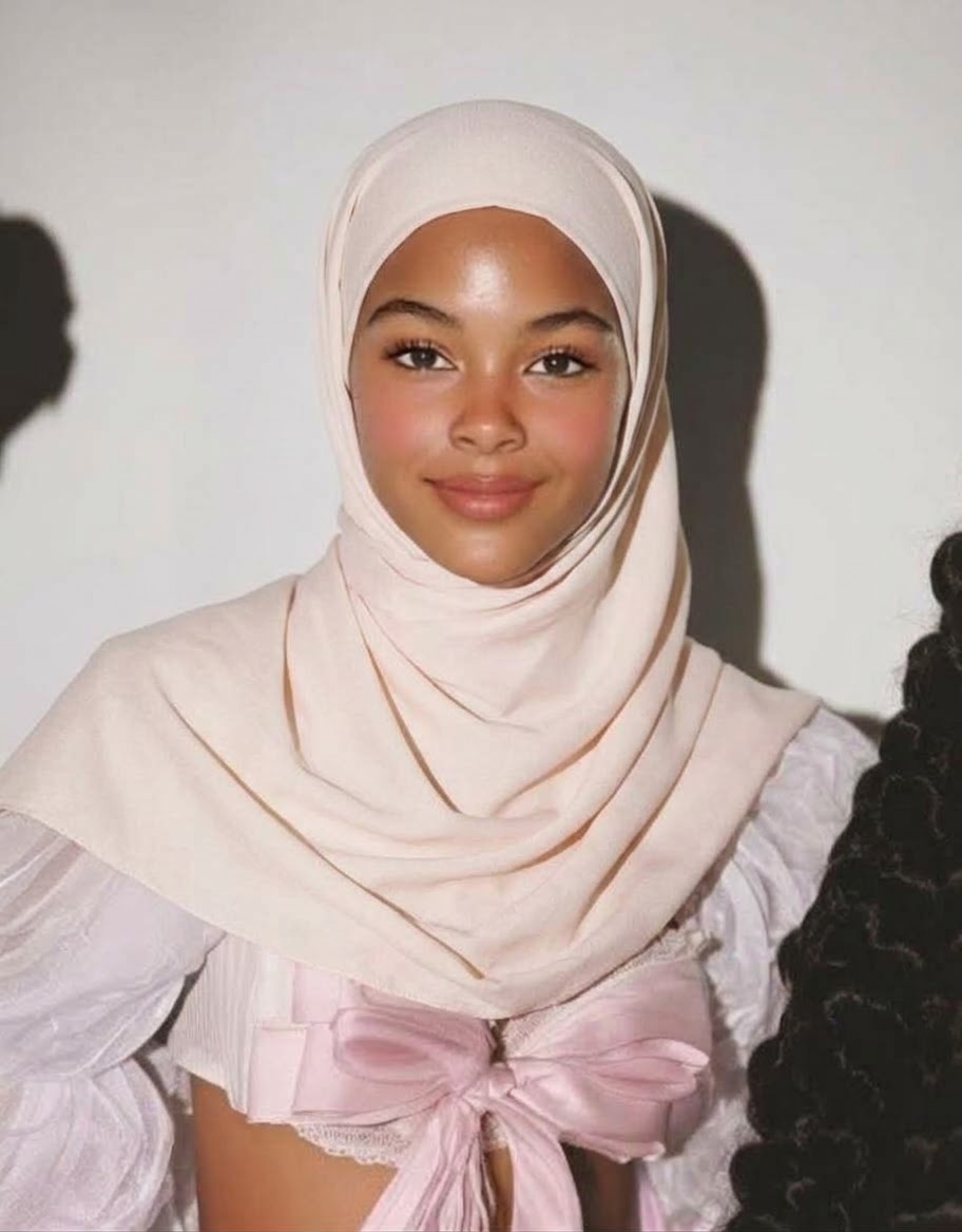 Blush hijab with a white undercap and pink bow-front top beside a sunlit pale wall.